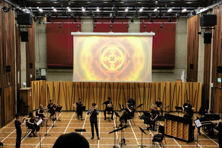 Music students perform with a large video projection on a screen in the background